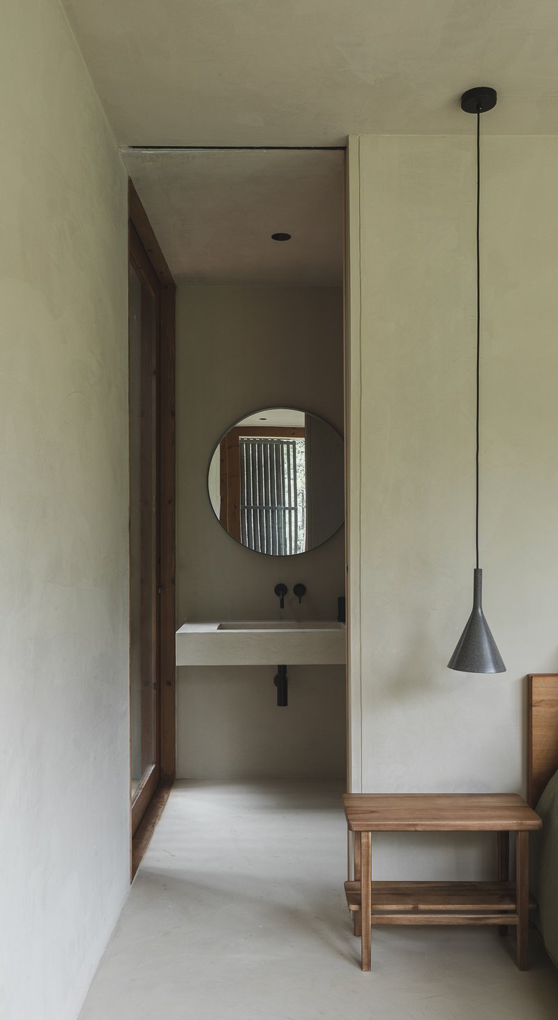 View through narrow hallway to bathroom with circular mirror and vertical timber screen beyond