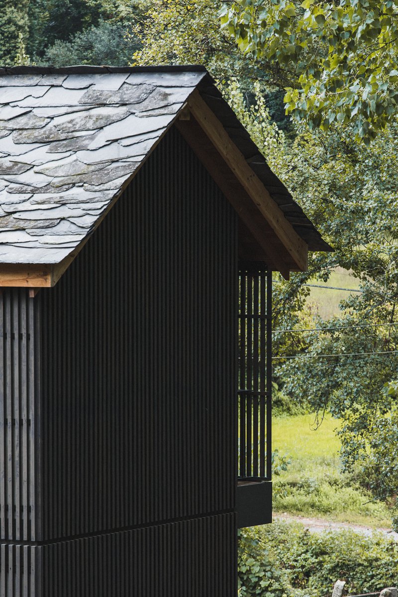 Gable end with black corrugated siding and vertical timber louvers beneath stone slate roof
