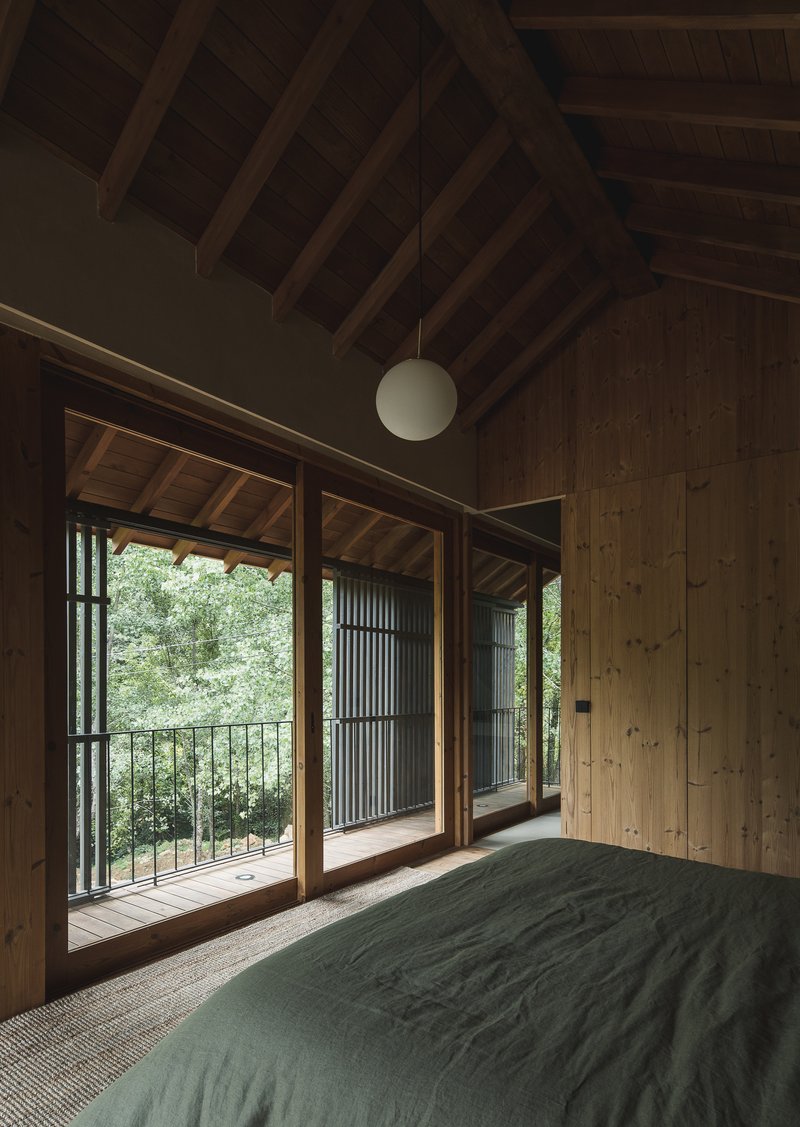 Timber bedroom interior with exposed rafters and glass doors opening to railing balcony