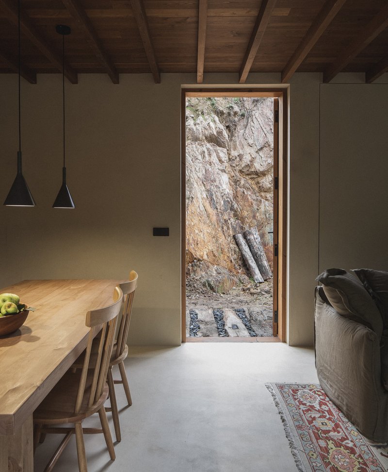 Tall narrow doorway framing weathered rock face with timber ceiling beams above dining table