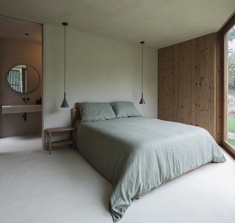 Bedroom with timber-clad wall and ensuite bathroom visible through doorway with circular mirror
