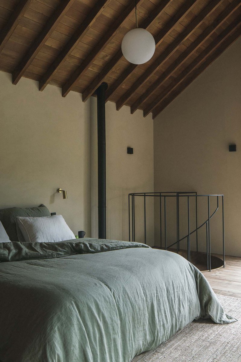 Bedroom with exposed timber rafters and steel railing at mezzanine edge in afternoon light