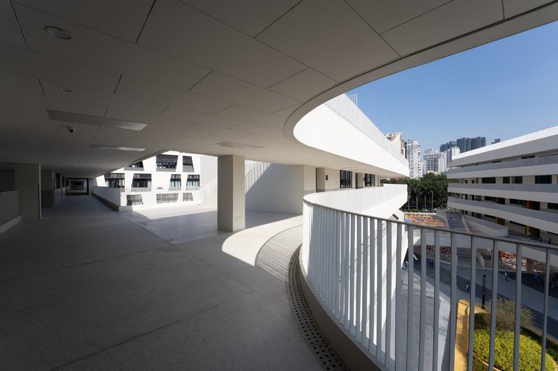 Covered walkway with curved concrete soffit and white vertical balustrade overlooking courtyard buildings