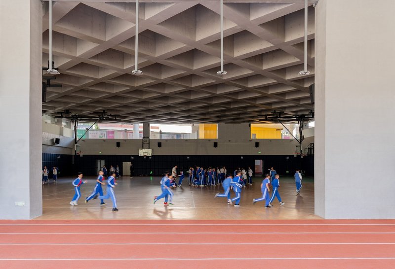 Indoor gymnasium with coffered concrete ceiling and students playing basketball on wood floor