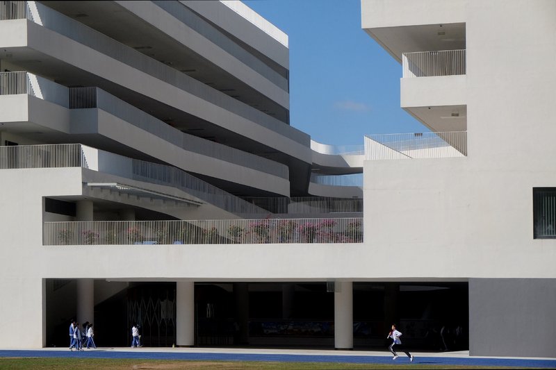 White stepped balconies facing a ground-level colonnade with pedestrians and a jogger on the lawn