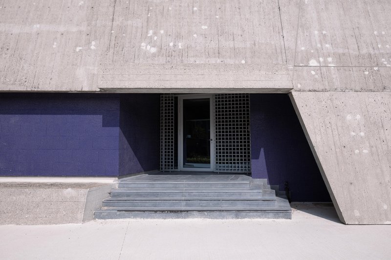 Sunken concrete entry stairs leading to recessed doors with metal grilles under bright midday sun