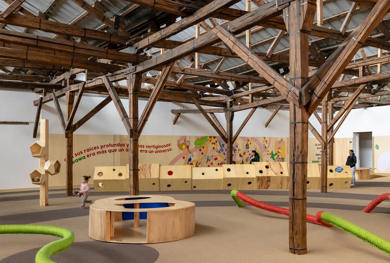 Wide view of the gallery showing timber columns, circular plywood seating and children running across the floor