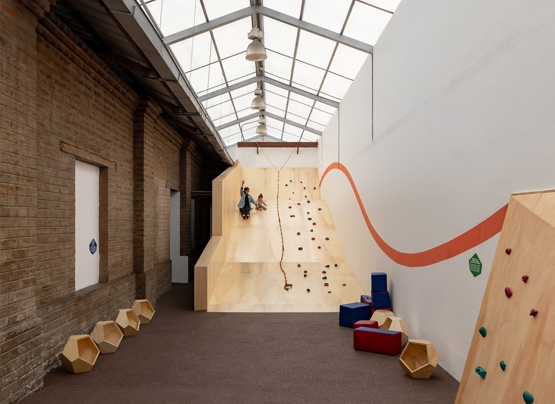 Interior play space with plywood climbing walls and glazed skylight above exposed brick walls