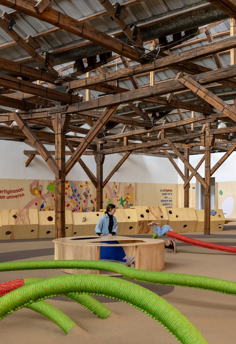 Interior view of exposed timber truss ceiling with translucent panels above play area with children