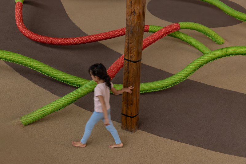 Child walking past timber column with green and red rope tubes extending across floor