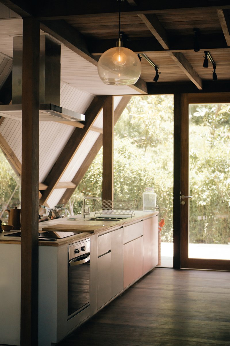 Kitchen island with white cabinetry beneath exposed timber beams and glass pendant fixture looking toward garden