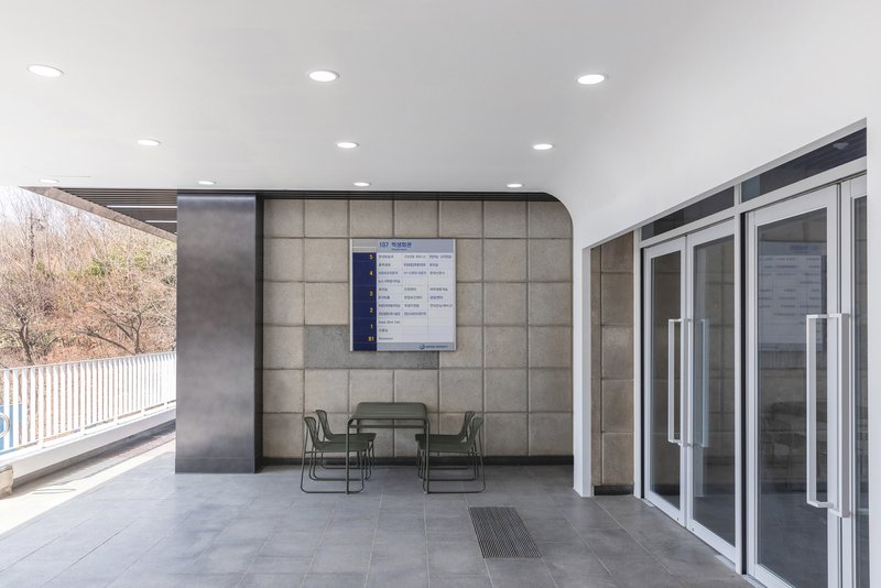 Covered outdoor terrace with metal seating, tiled floor and information board on textured wall