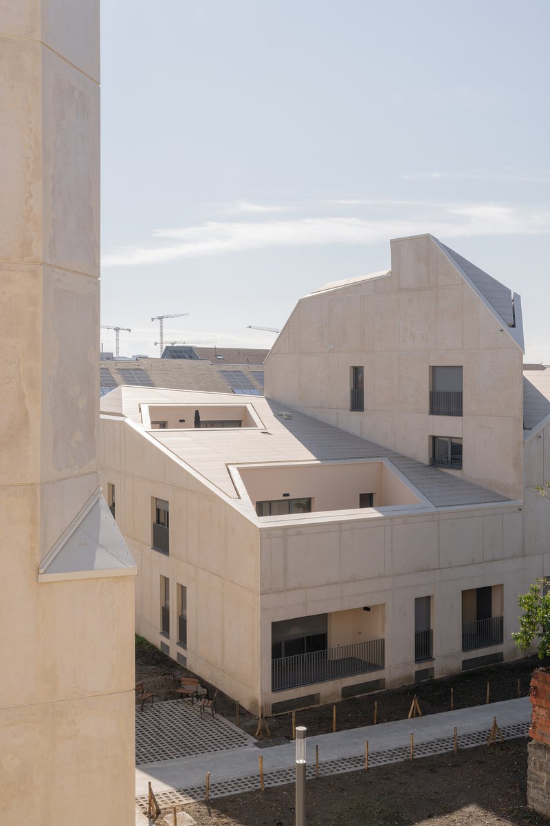 Pale concrete facade with staggered roofline and punched window openings under an overcast sky