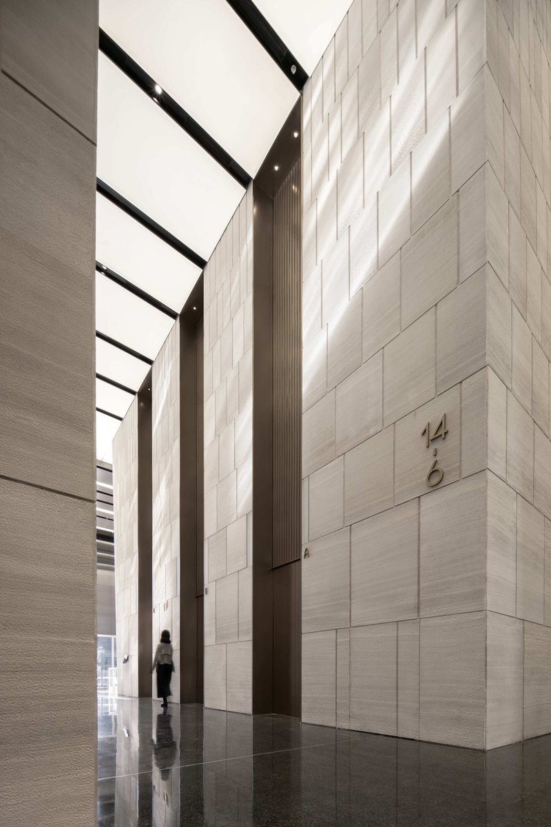 Tall lobby with pale stone block walls and a skylight casting natural light onto a polished floor