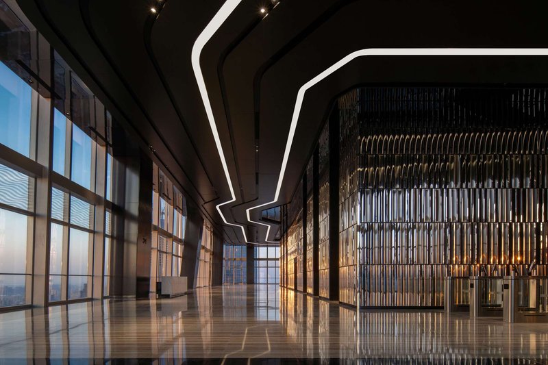 Corner lobby view showing curtain wall, decorative metal screen partition and angular ceiling light at twilight