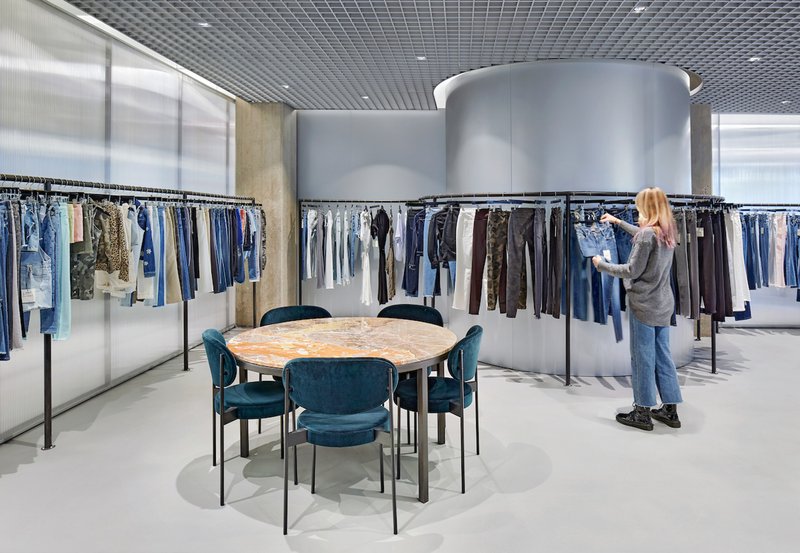 Open showroom floor with clothing racks arranged around silver cylindrical volumes and grey grid ceiling