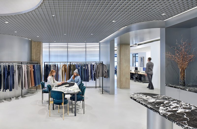 View through showroom space showing clothing displays and marbled reception desk with dried branch arrangement