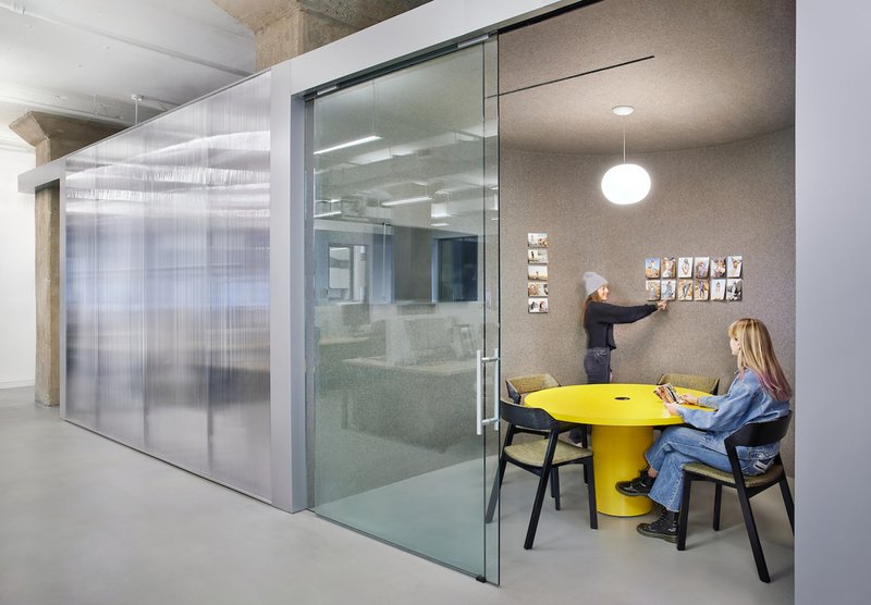 Meeting nook with yellow table adjacent to translucent sliding glass partition and cork pinboard wall