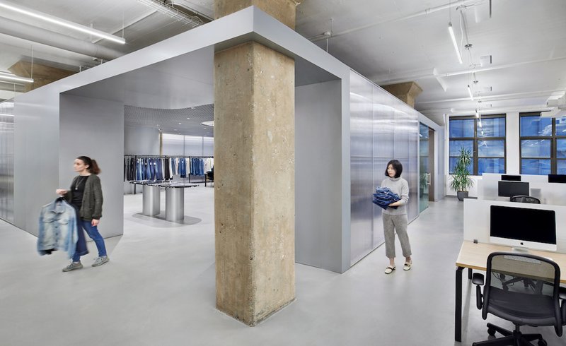 Open office floor with exposed concrete column framed by grey partitions and people in motion