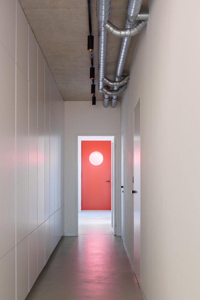 Narrow hallway with exposed ductwork on the ceiling and red door with circular window at end