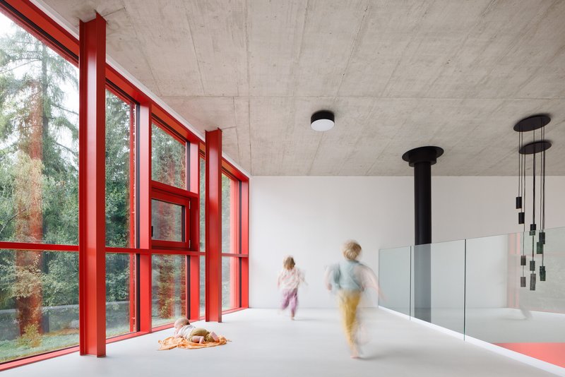 Interior with red window mullions, exposed concrete ceiling, and two figures in motion blur