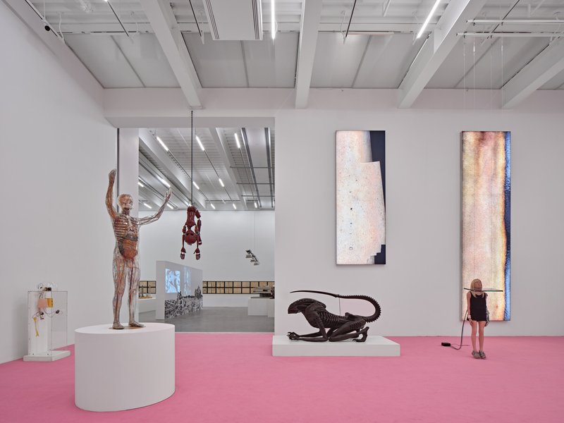 Gallery interior with pink resin floor, white walls, exposed ceiling beams, and visitors among sculptural works