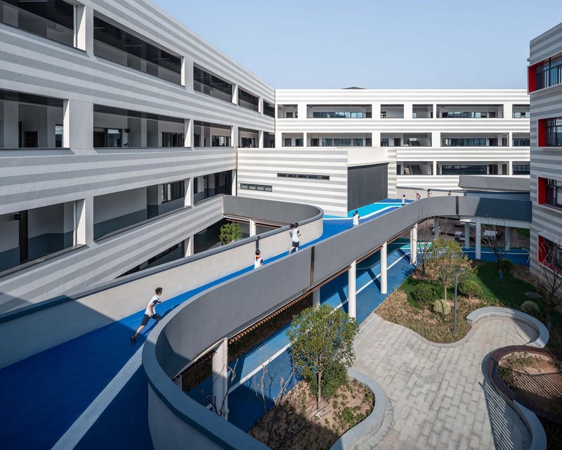 Elevated blue running track curving between striped facade buildings with planted beds below