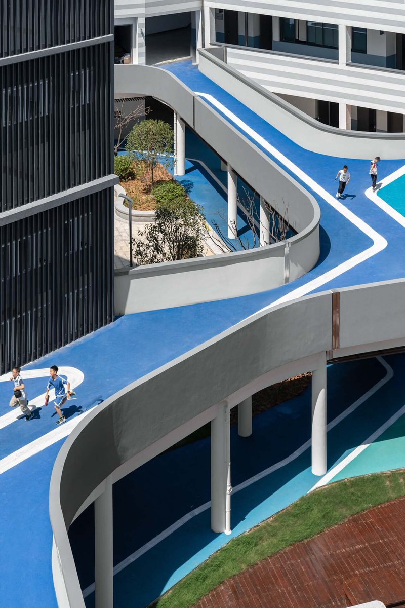Elevated running track winding between planted beds and columns with students gathering below