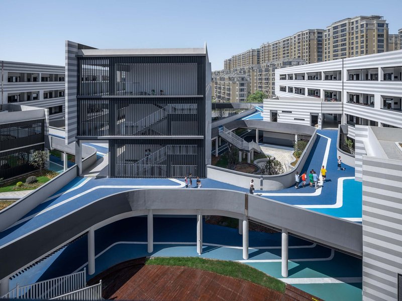 Aerial view of curved pedestrian bridges with blue surfacing linking horizontal striped buildings around a central courtyard