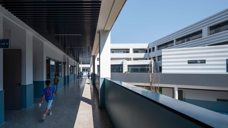 Open-air corridor with slatted black ceiling overlooking a courtyard where children walk in afternoon light