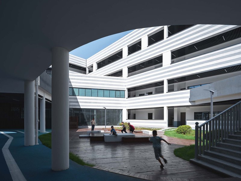 Ground-level courtyard with timber deck and lawn where children play beneath curved horizontal striped facades