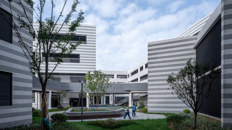 Courtyard with circular seating element and horizontal striped facades framed by trees and planted beds