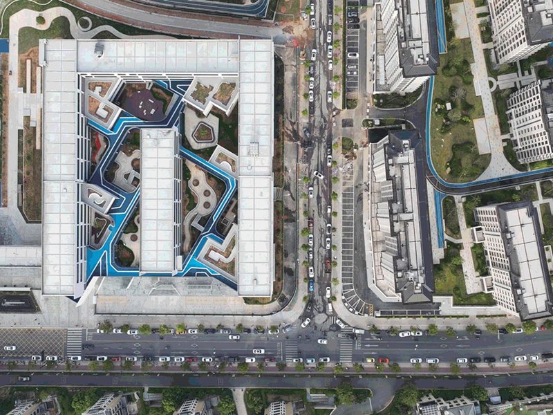 Drone view of rooftop with blue courtyard pattern surrounded by city streets and traffic