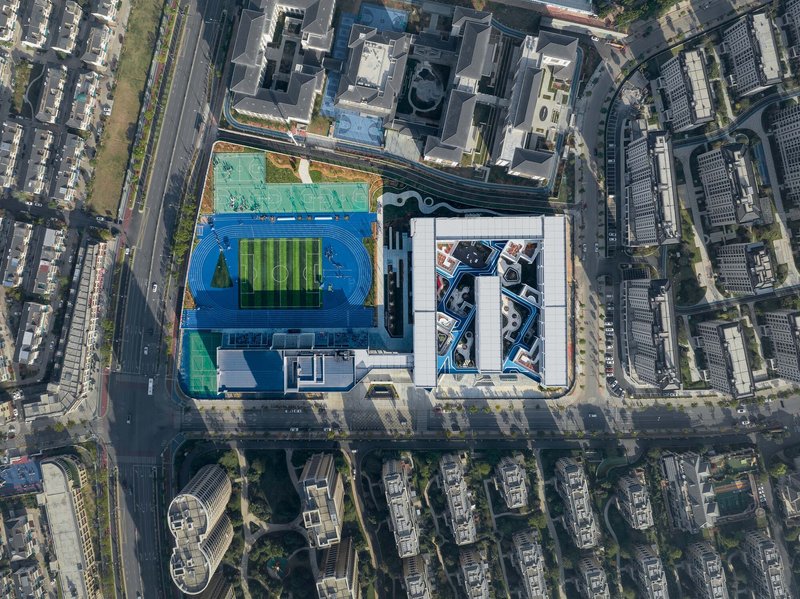 Aerial view of the campus with blue running track and rooftop sports field surrounded by urban blocks
