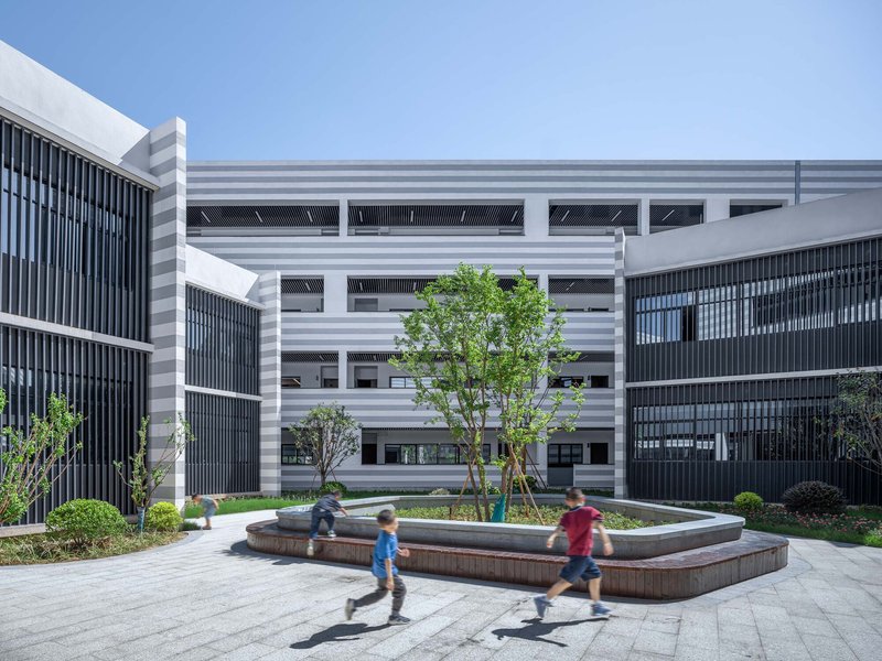 Central courtyard with circular fountain and children running past planted trees between striped facades