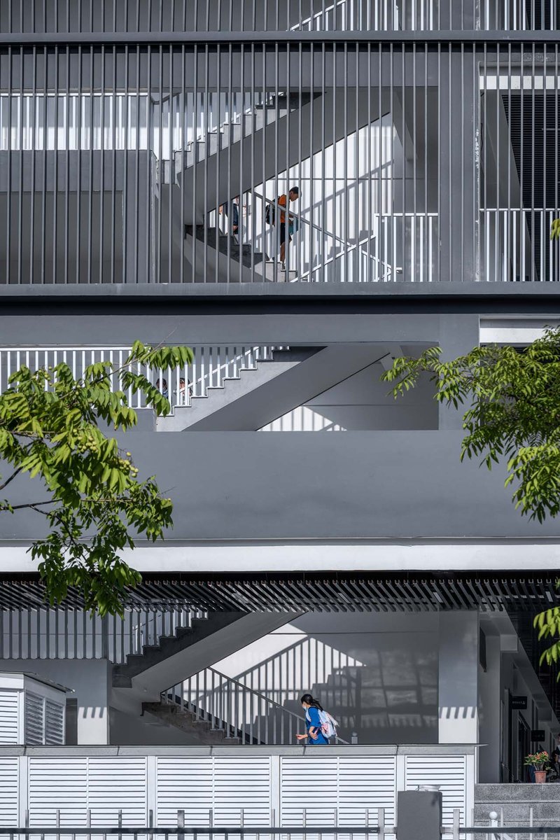 Stacked exterior staircases with vertical metal screening creating shadow patterns as a child descends