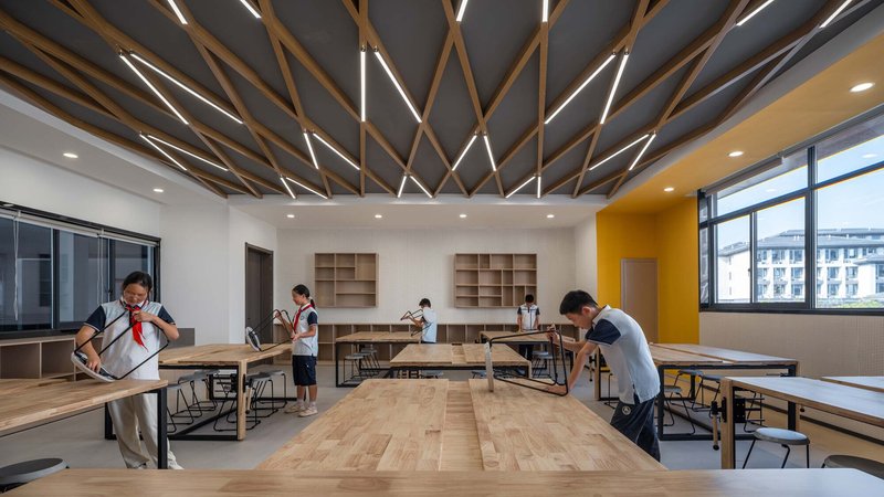 Interior classroom with diagonal timber ceiling beams and integrated linear lighting above students at work tables