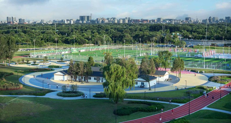 Elevated view of circular pathway surrounding white pavilion with willow trees and sports fields beyond