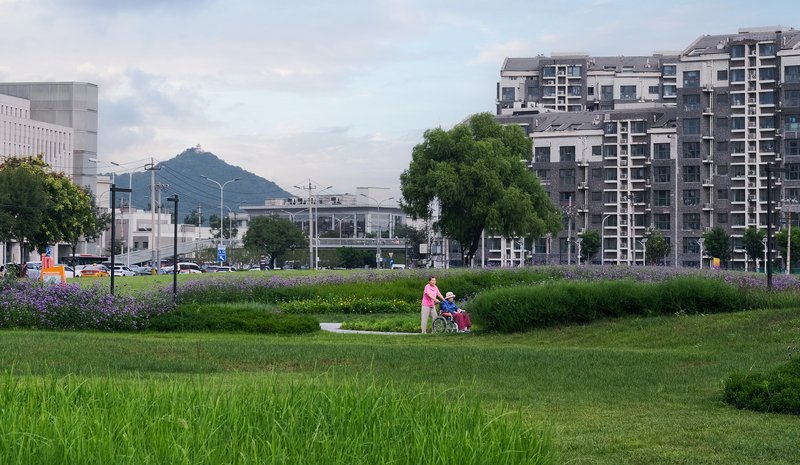 Lawn and planted beds with two people sitting beside a distant mountain backdrop and residential towers