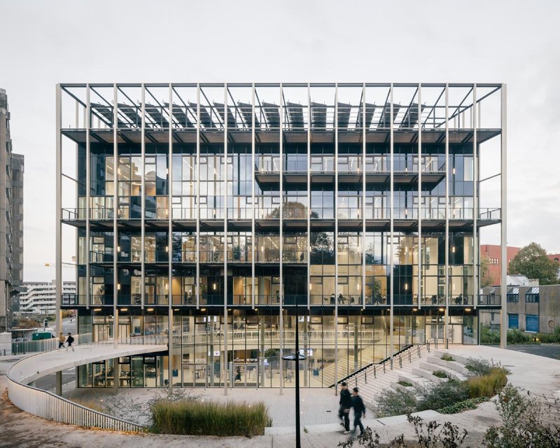 Street facade: glass-and-steel cube with a vertical timber fin rhythm, exterior stair amphitheatre rising from a sunken planted landscape, people at the entry
