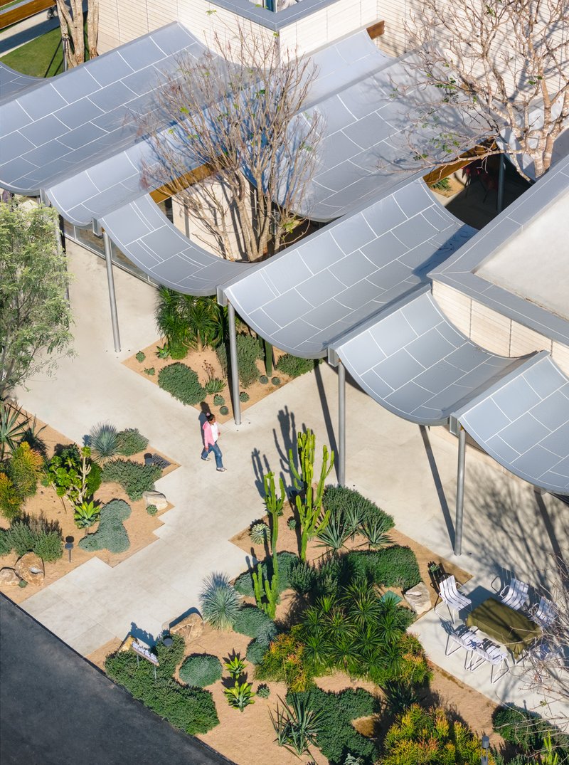 Top-down view of undulating tiled canopy with a planted courtyard and two figures below