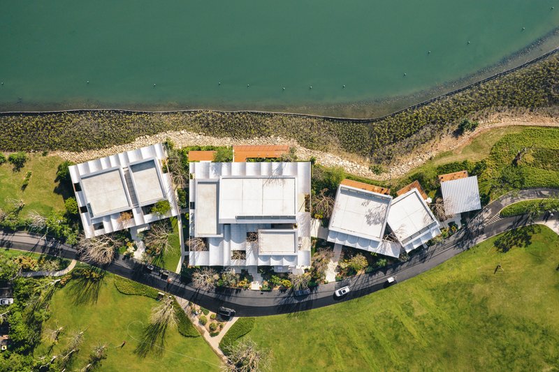 Drone view of three clustered white-roofed structures between a canal and grass field
