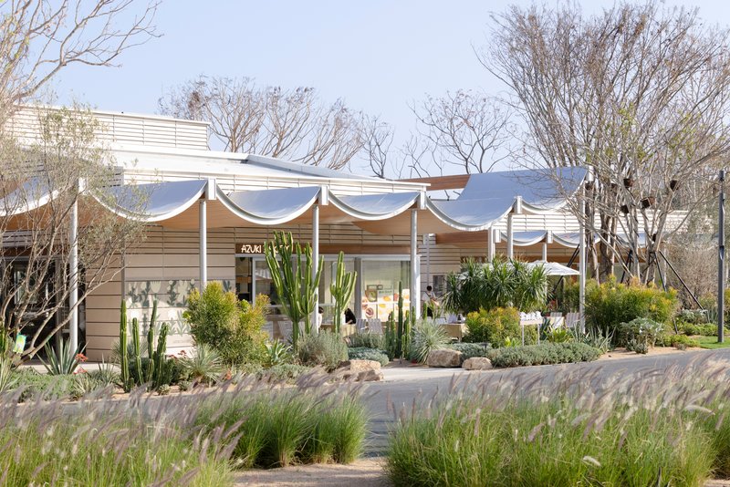 Fabric canopy with white columns shading a glazed pavilion surrounded by cacti and desert grasses