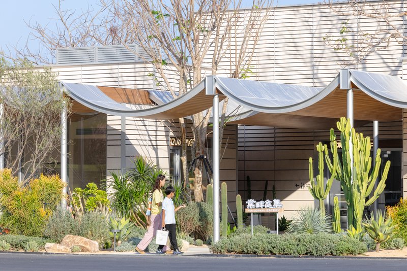 Two visitors walking beneath a scalloped fabric canopy beside a horizontal wood clad facade