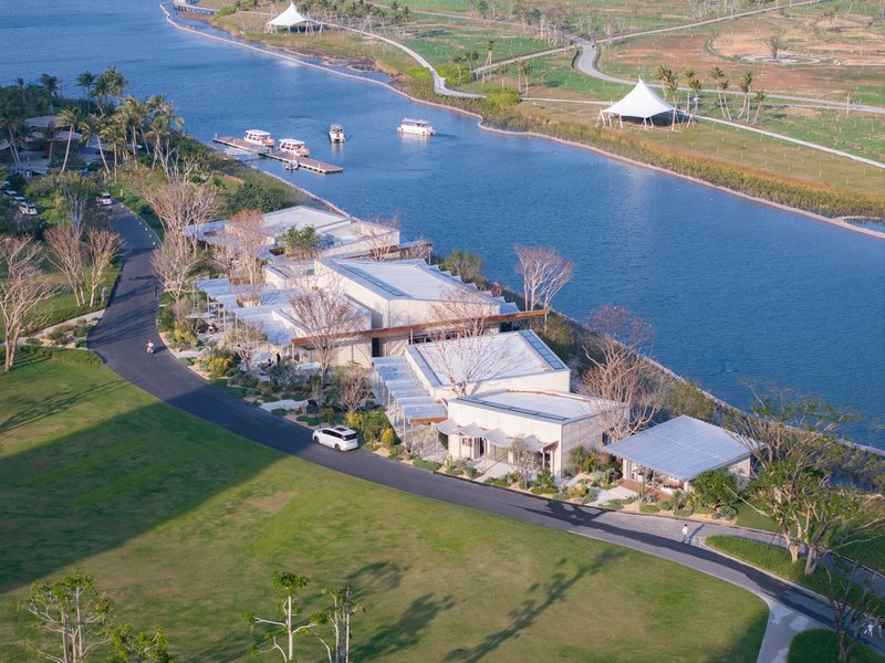 Aerial view of white flat-roofed volumes clustered along a canal with boats and palm trees