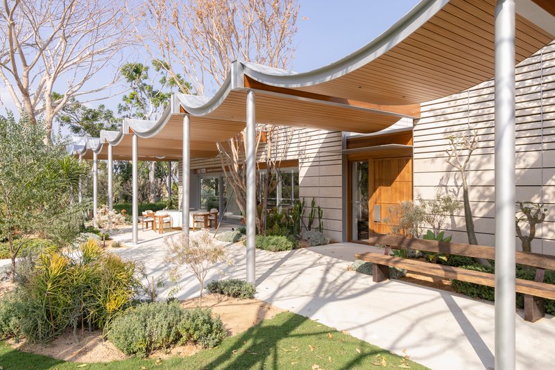 Covered terrace with undulating wood ceiling and white columns framing a landscaped courtyard with bare trees