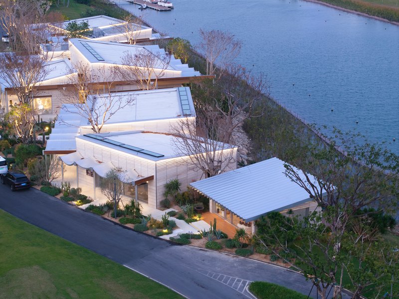 Aerial view of corrugated metal roofs cascading down a planted slope toward the water at dusk