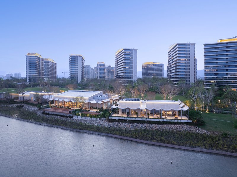 Evening view of white undulating roofs along the lake edge with illuminated high-rise towers beyond