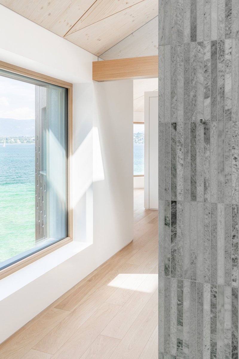 Hallway corner with deep window niche framing lake views and striped vertical concrete panel beside timber ceiling