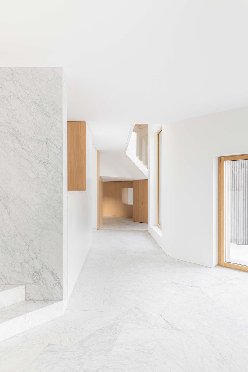 White marble stair beside timber cabinet opening into double height space with angled skylight above